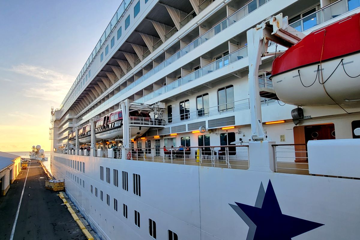 Pride of America alongside the pier at golden hour, with balconies and lifeboats above the quay
