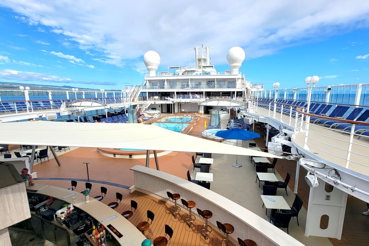 The pool deck of Pride of America by day, with loungers, bar and open ocean beyond