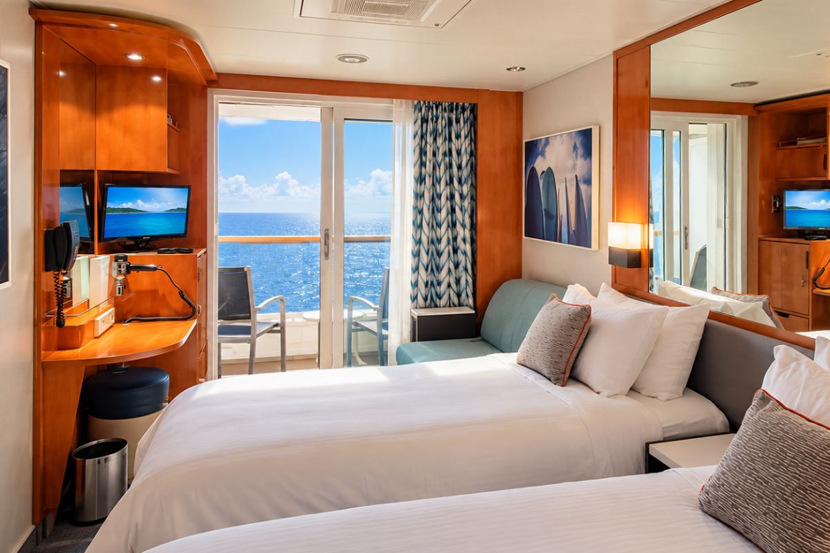 A balcony cabin on Pride of America made up with two single beds, balcony door open to the ocean