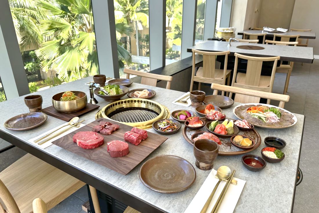 A table set with the tabletop grill, raw beef and side dishes by the windows at Onkee