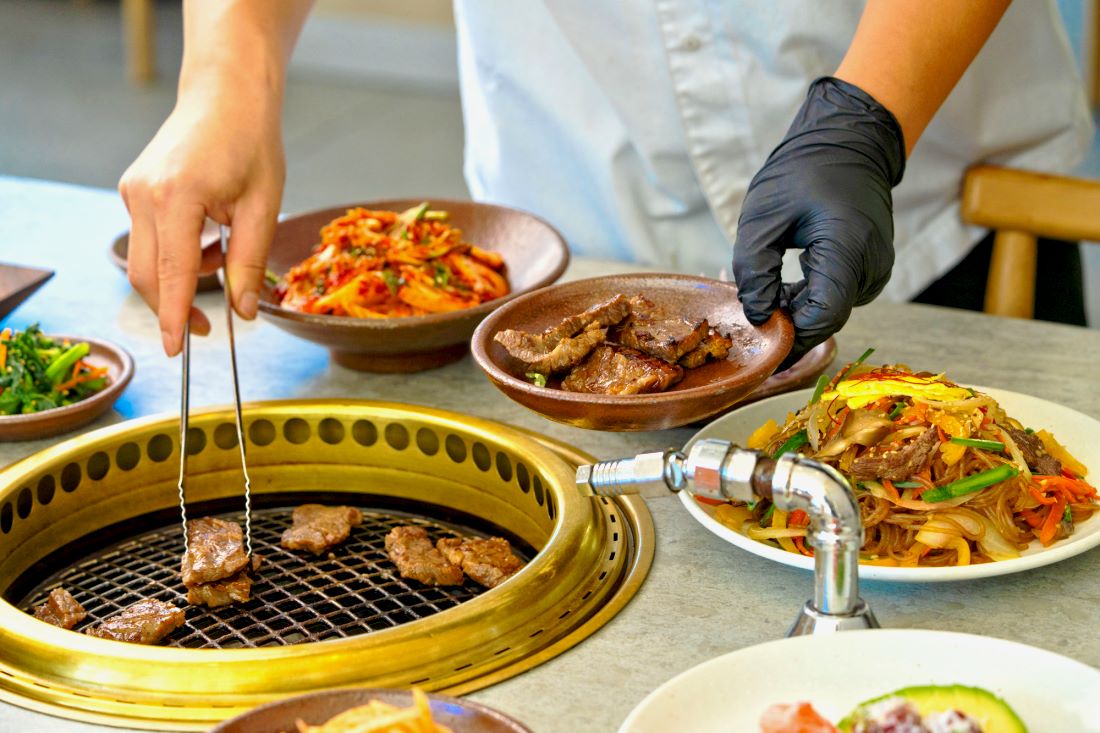 Beef grilling on the tabletop grill at Onkee, with kimchi and japchae alongside