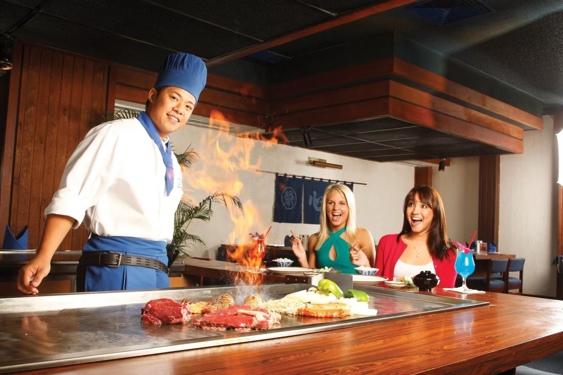 A teppanyaki chef at the griddle with guests seated around it