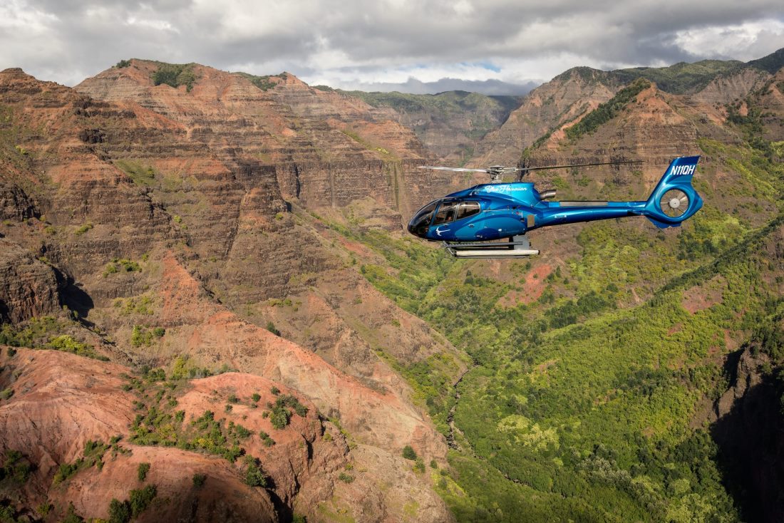 A Blue Hawaiian helicopter banking over the red cliffs of Waimea Canyon on Kauai