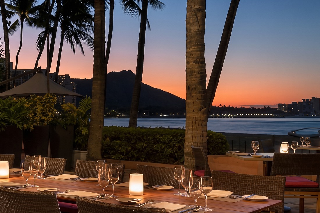 Candlelit oceanfront tables at Azure at sunset, with Diamond Head and the Waikiki shoreline