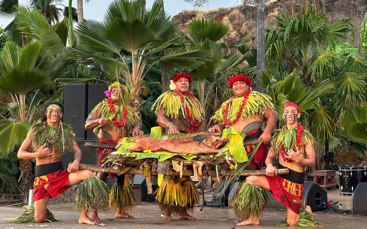 Performers in ti leaf skirts presenting the whole roast pig on a platter at Chiefs Luau