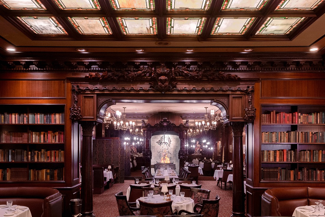 The dark wood dining room at Hy's Steak House, with bookshelves, stained glass ceiling panels and a fireplace