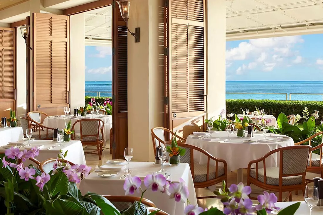 White-clothed tables and orchids in the open-air dining room at Orchids, looking out to the ocean