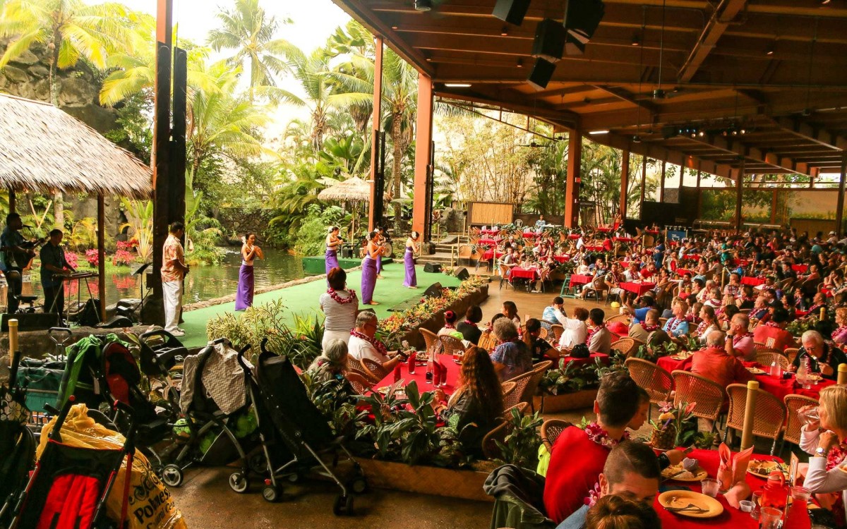 The open-air luau pavilion at the Polynesian Cultural Center filled with guests at red-clothed tables