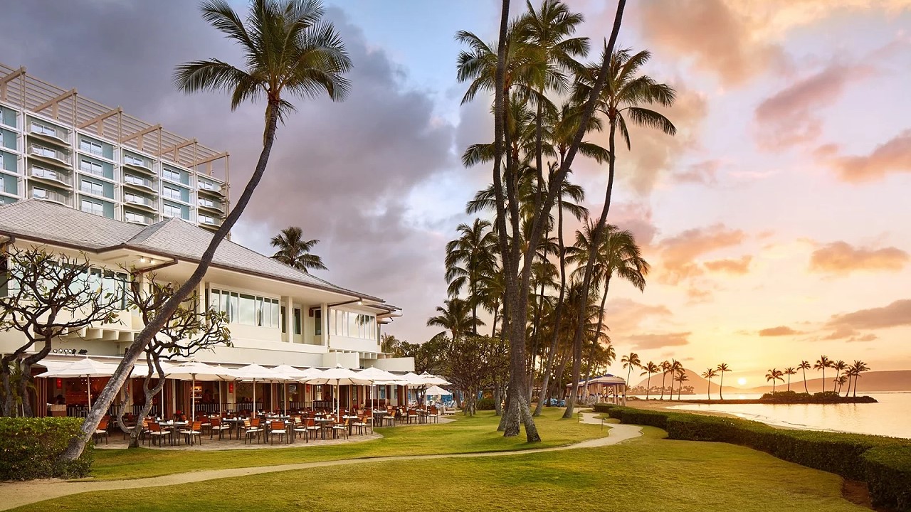 The Kahala at sunset, with the terrace umbrellas of Plumeria Beach House on the lawn beside the beach
