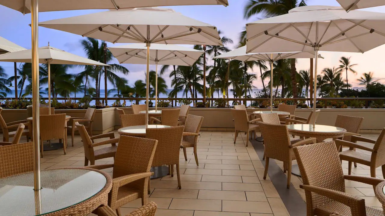 The open-air terrace at The Buffet at Hyatt at dusk, with umbrellas, palms and the ocean beyond